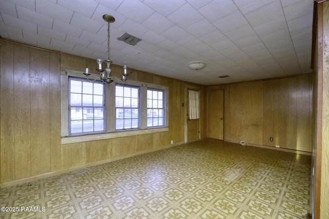 spare room with a notable chandelier, baseboards, light floors, and wood walls