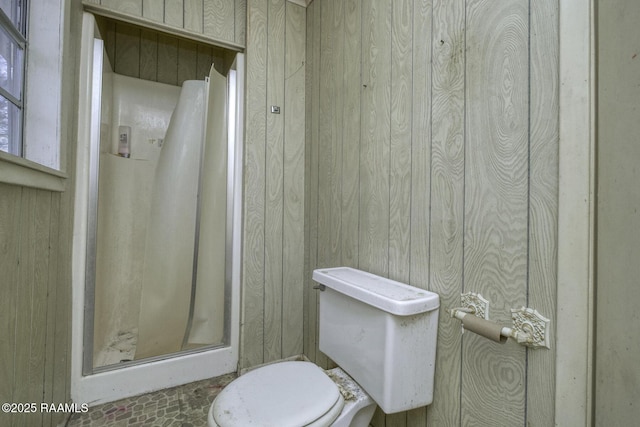 bathroom with wooden walls, a shower stall, and toilet