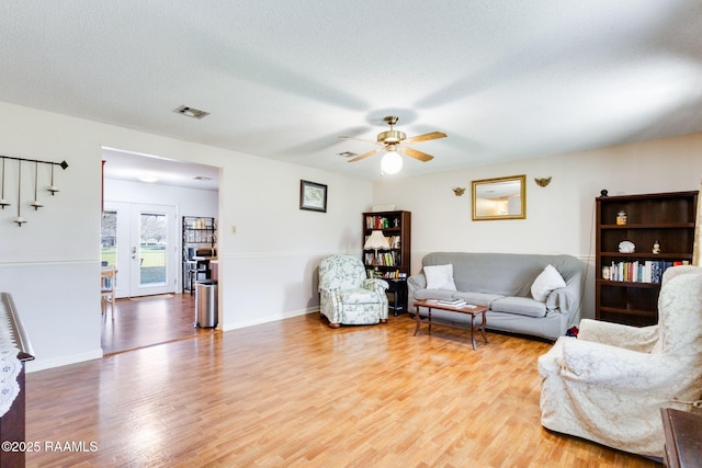 living room with visible vents, a textured ceiling, baseboards, and wood finished floors