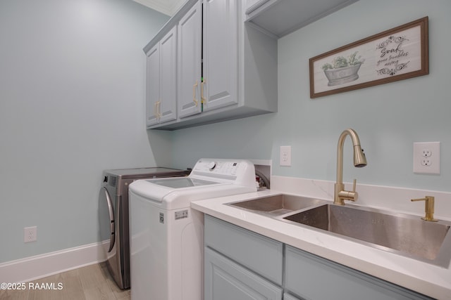 laundry area featuring baseboards, light wood-style flooring, washer and dryer, cabinet space, and a sink