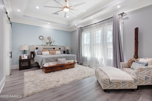 bedroom featuring a barn door, recessed lighting, a raised ceiling, and ornamental molding