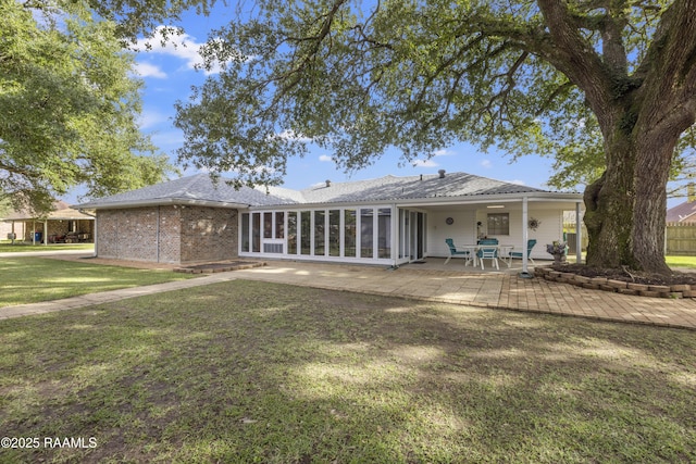 rear view of property with a yard, a sunroom, brick siding, and a patio area