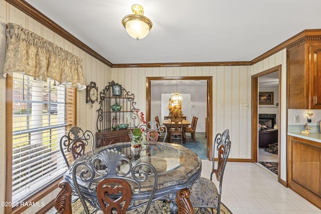 dining space with baseboards, wallpapered walls, light tile patterned flooring, a fireplace, and crown molding