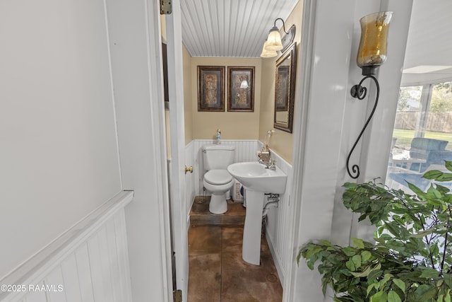 half bath featuring a sink, a decorative wall, toilet, and wainscoting