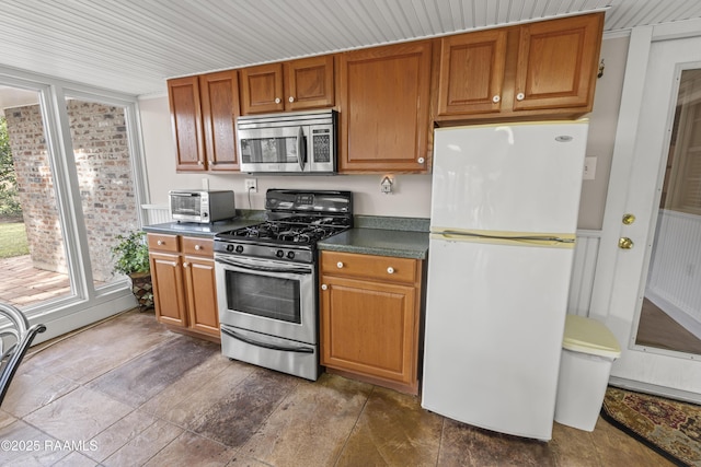 kitchen featuring dark countertops, appliances with stainless steel finishes, brown cabinetry, and a toaster