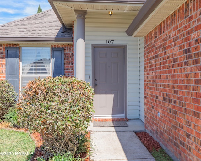 doorway to property featuring brick siding and a shingled roof