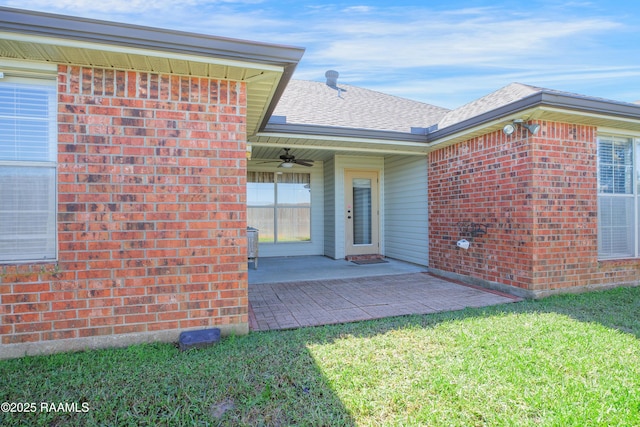 property entrance featuring a yard, a shingled roof, brick siding, ceiling fan, and a patio area