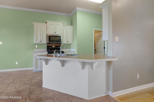 kitchen with a breakfast bar area, black range, crown molding, white cabinetry, and stainless steel microwave