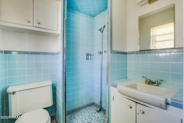 bathroom featuring toilet, a tile shower, tile walls, wainscoting, and vanity