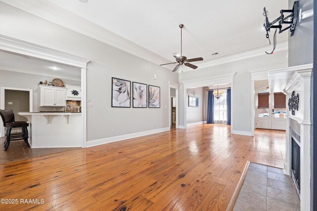 living area with visible vents, light wood-style flooring, ornamental molding, ceiling fan with notable chandelier, and baseboards