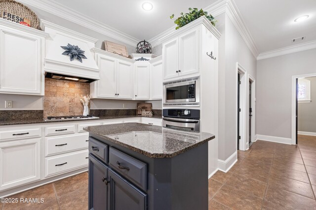 kitchen featuring dark stone countertops, a kitchen island, stainless steel appliances, white cabinets, and crown molding