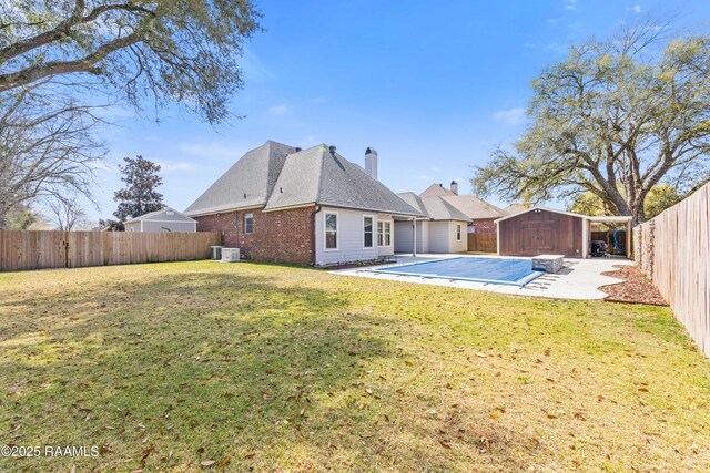 back of house featuring brick siding, a lawn, an outdoor structure, a fenced backyard, and a patio