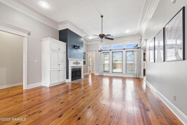 unfurnished living room with light wood-type flooring, ornamental molding, a tiled fireplace, baseboards, and ceiling fan