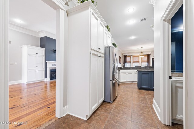 kitchen with visible vents, crown molding, white cabinetry, dark countertops, and stainless steel fridge