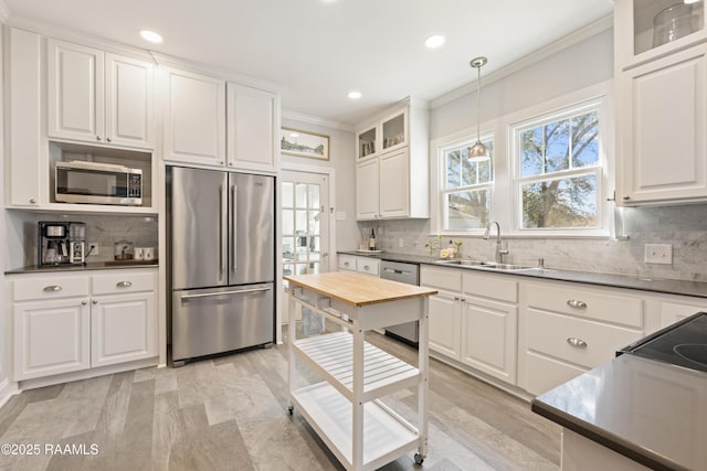 kitchen featuring ornamental molding, a sink, white cabinetry, stainless steel appliances, and glass insert cabinets