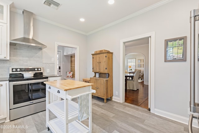 kitchen featuring visible vents, decorative backsplash, stainless steel range with electric cooktop, arched walkways, and wall chimney exhaust hood