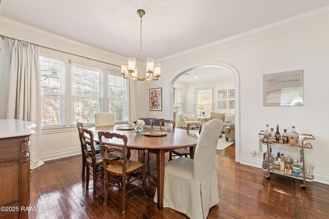 dining space with dark wood finished floors, arched walkways, a wealth of natural light, and ornamental molding