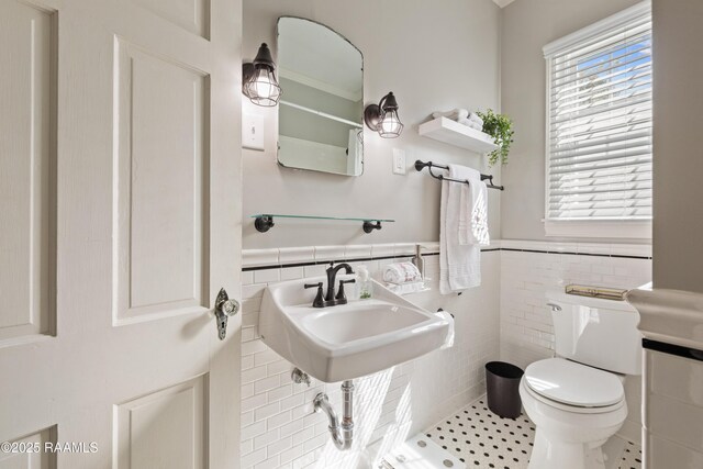 bathroom featuring a wealth of natural light, wainscoting, toilet, and tile walls