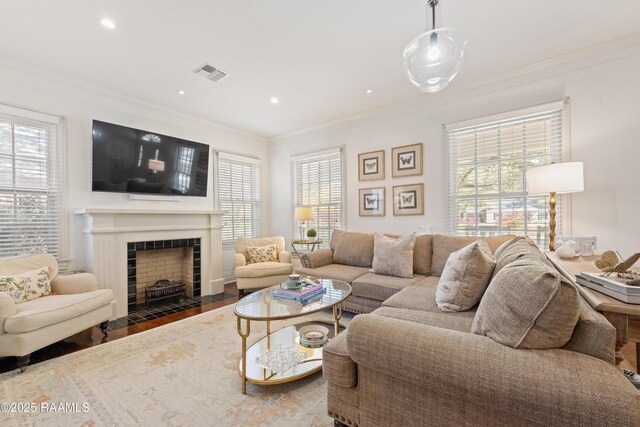 living area with visible vents, a healthy amount of sunlight, wood finished floors, and crown molding