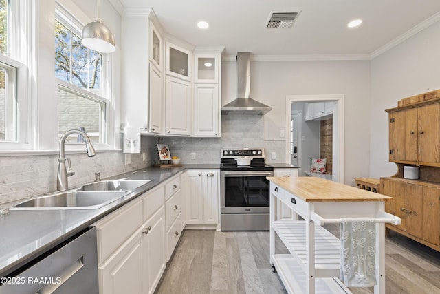 kitchen with visible vents, a sink, ornamental molding, stainless steel appliances, and wall chimney range hood