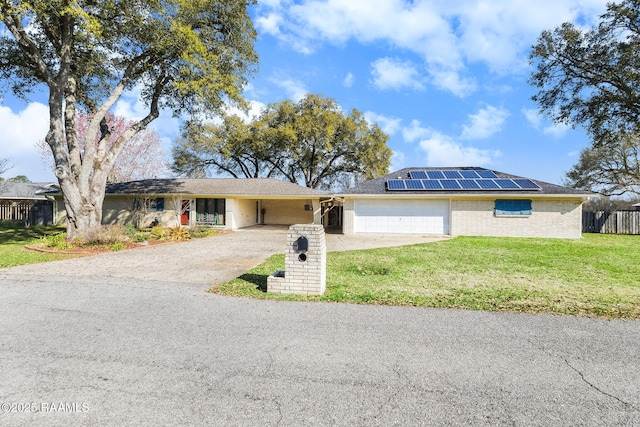 ranch-style home with driveway, fence, a front yard, brick siding, and solar panels