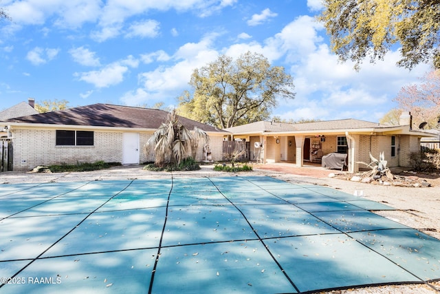 back of property with a covered pool, brick siding, a chimney, and a patio area