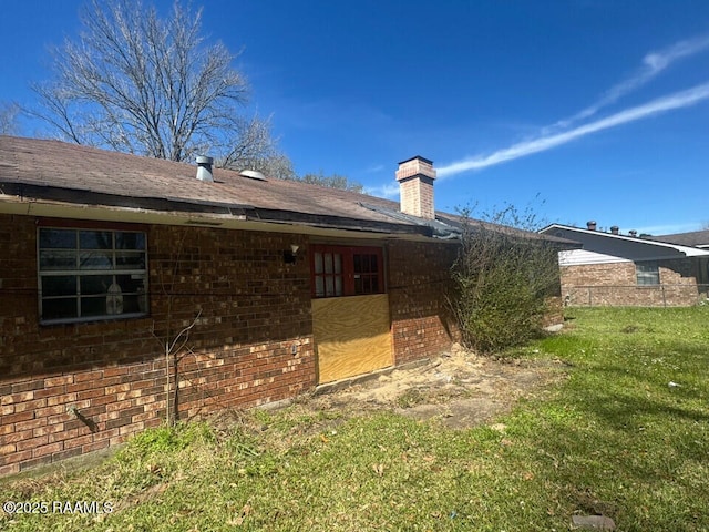 back of house with brick siding, a chimney, and a lawn