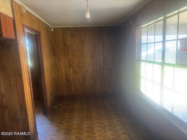 interior space featuring wooden walls, a healthy amount of sunlight, crown molding, and a textured ceiling