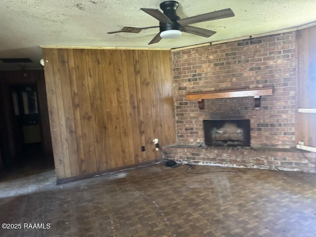 unfurnished living room featuring a ceiling fan, wooden walls, a fireplace, and a textured ceiling