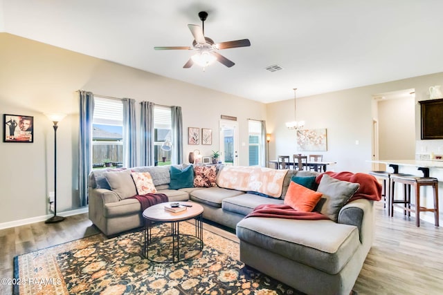 living area featuring light wood-type flooring, visible vents, baseboards, and ceiling fan with notable chandelier