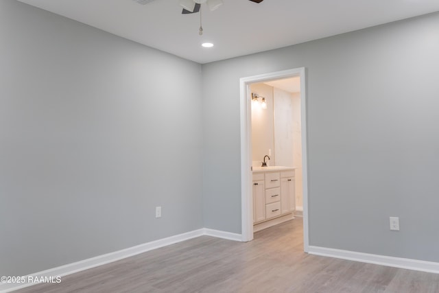 empty room featuring indoor wet bar, light wood-style flooring, a ceiling fan, and baseboards