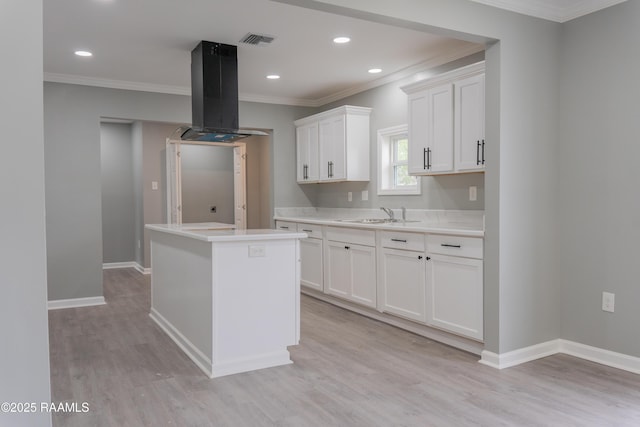 kitchen with visible vents, ornamental molding, island exhaust hood, light wood-style floors, and a sink