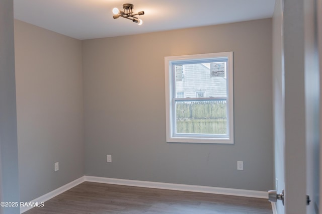 empty room featuring dark wood-style floors, baseboards, and a chandelier