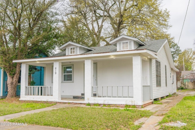 bungalow-style home with a front yard, covered porch, and roof with shingles