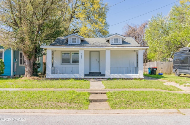 bungalow-style house with a front lawn, fence, covered porch, and a shingled roof