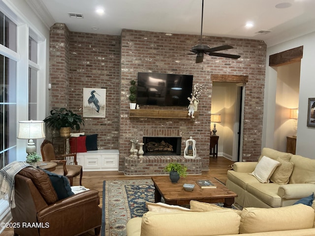 living area featuring visible vents, wood finished floors, a brick fireplace, and ceiling fan