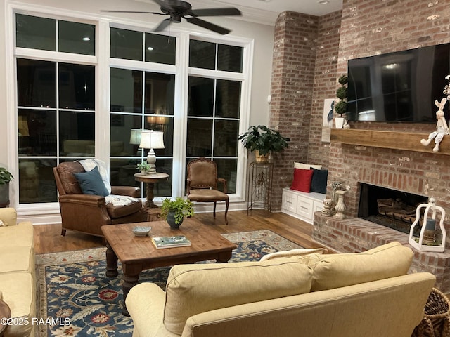 living area with a fireplace, wood finished floors, crown molding, and a ceiling fan