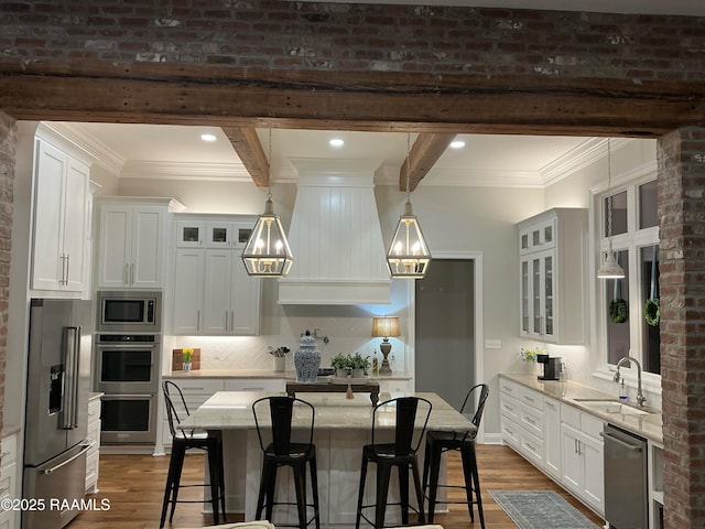 kitchen featuring a kitchen bar, a sink, wood finished floors, white cabinetry, and appliances with stainless steel finishes