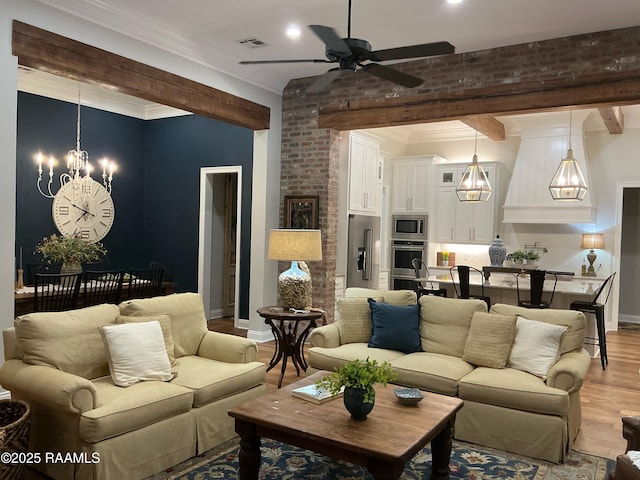 living area featuring visible vents, baseboards, ornamental molding, ceiling fan with notable chandelier, and light wood-type flooring