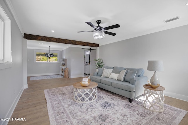 living area with visible vents, baseboards, light wood-style flooring, a barn door, and ceiling fan with notable chandelier