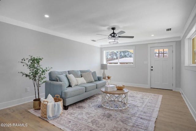 living room with visible vents, baseboards, light wood-style floors, and ornamental molding