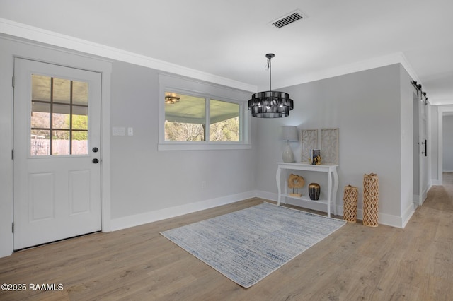 foyer entrance with a barn door, crown molding, visible vents, and a wealth of natural light