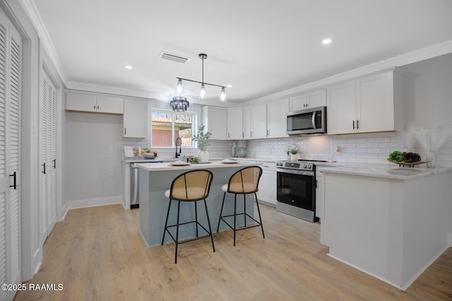 kitchen featuring visible vents, appliances with stainless steel finishes, light wood-type flooring, and a kitchen bar