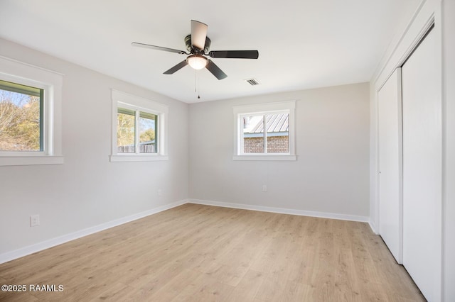 unfurnished bedroom featuring baseboards, light wood-type flooring, multiple windows, and a closet