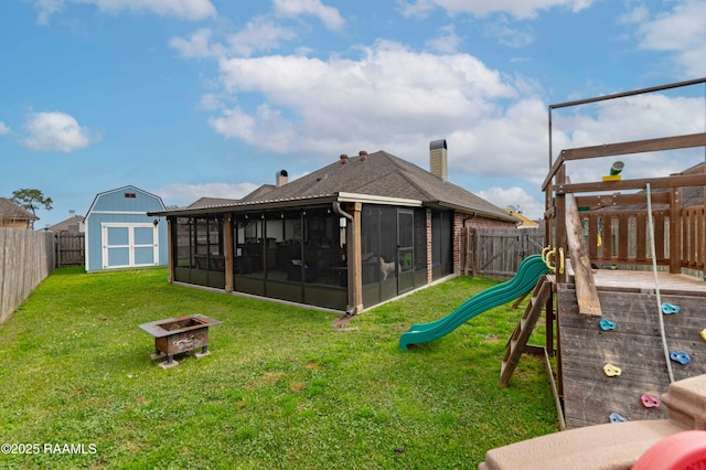 rear view of property with a shed, an outdoor fire pit, a fenced backyard, and a sunroom