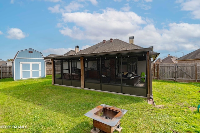 rear view of property featuring a storage unit, a fire pit, a lawn, and a sunroom