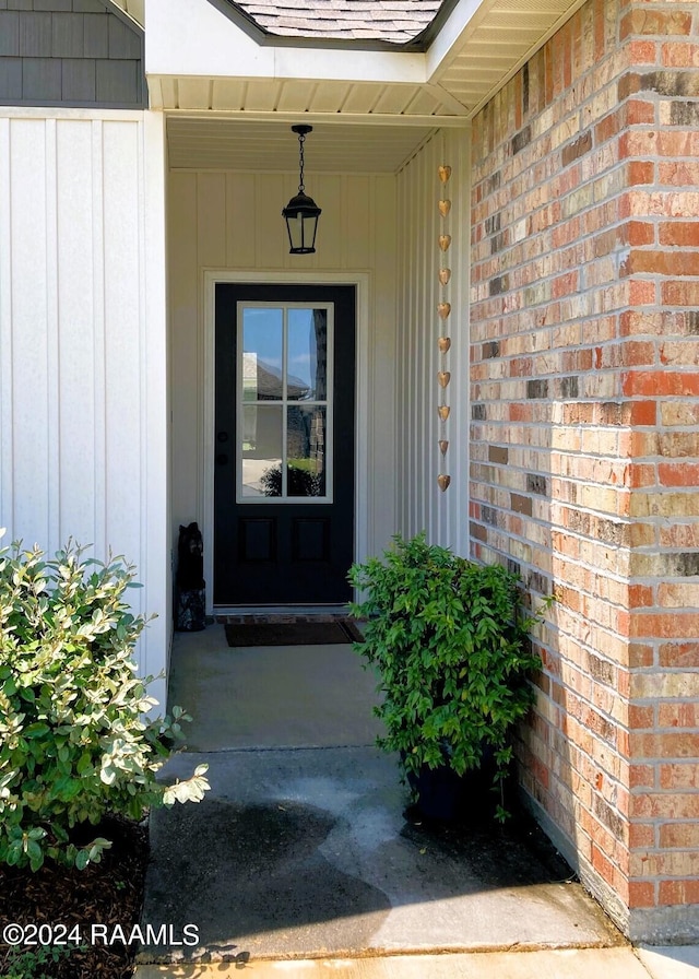 doorway to property featuring brick siding and roof with shingles