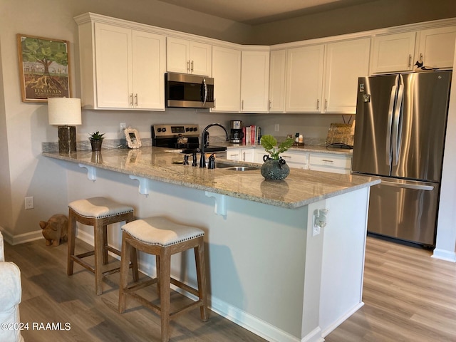 kitchen featuring light stone counters, light wood-style flooring, a peninsula, stainless steel appliances, and white cabinetry