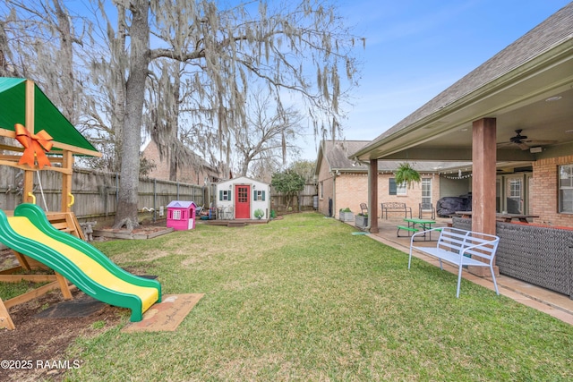 view of yard with an outbuilding, a ceiling fan, a fenced backyard, a shed, and a playground