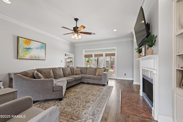 living area featuring a fireplace with flush hearth, dark wood-type flooring, ornamental molding, a ceiling fan, and baseboards